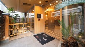 L'entrée d'un hôtel, avec un plafond en bois, des portes en verre et un paillasson sur lequel est inscrit le nom « ROY Group ».