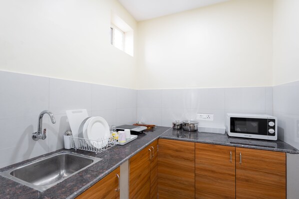 A kitchen with a granite countertop, stainless steel sink, wooden cabinets, a microwave, and a dish rack.