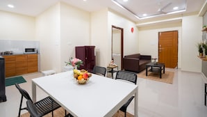 A modern living room with a dining table, chairs, a sofa, and a coffee table. There is a microwave in the kitchen area. - Iris At Nest (Hyderabad)