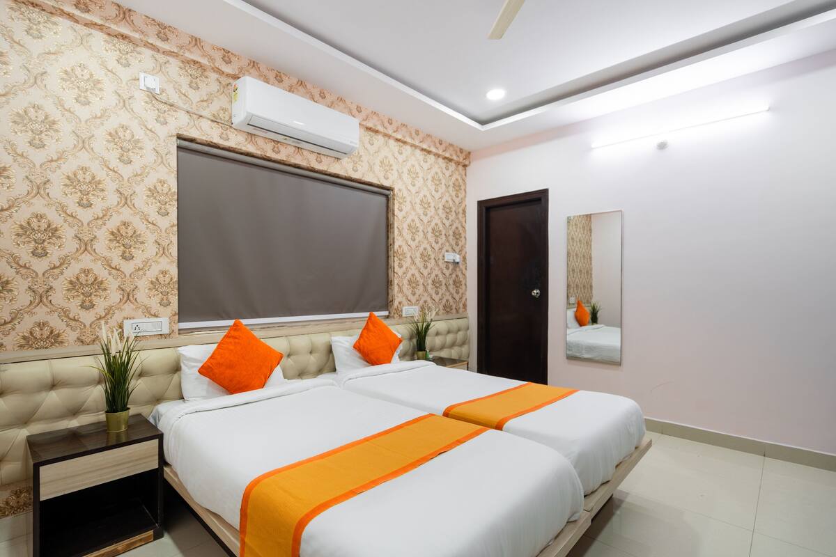 A hotel room with a large bed, two nightstands, a potted plant, an air conditioning unit, and a mirror on the wall.