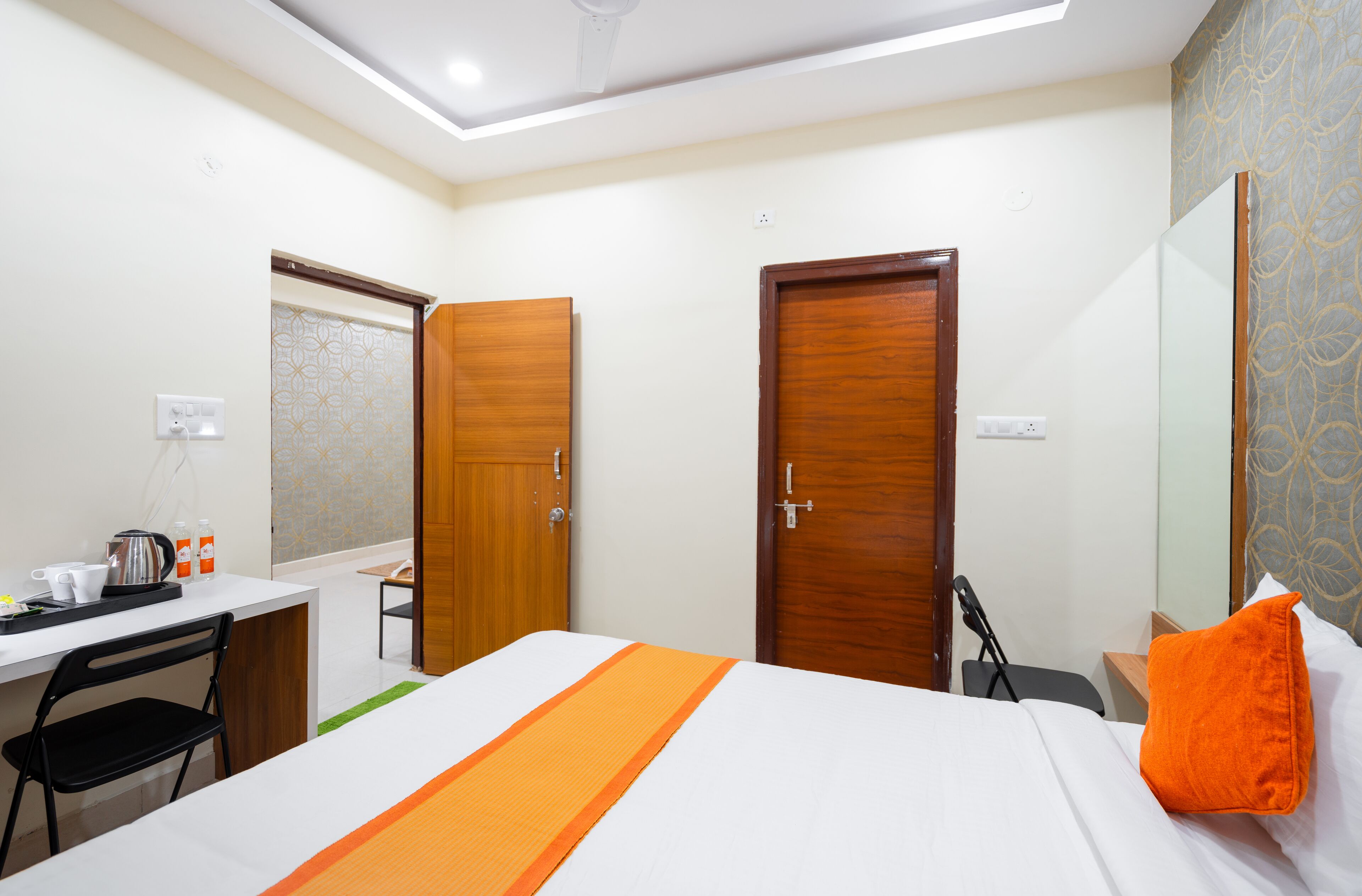 A hotel room with a bed, a desk, a chair, and two doors.