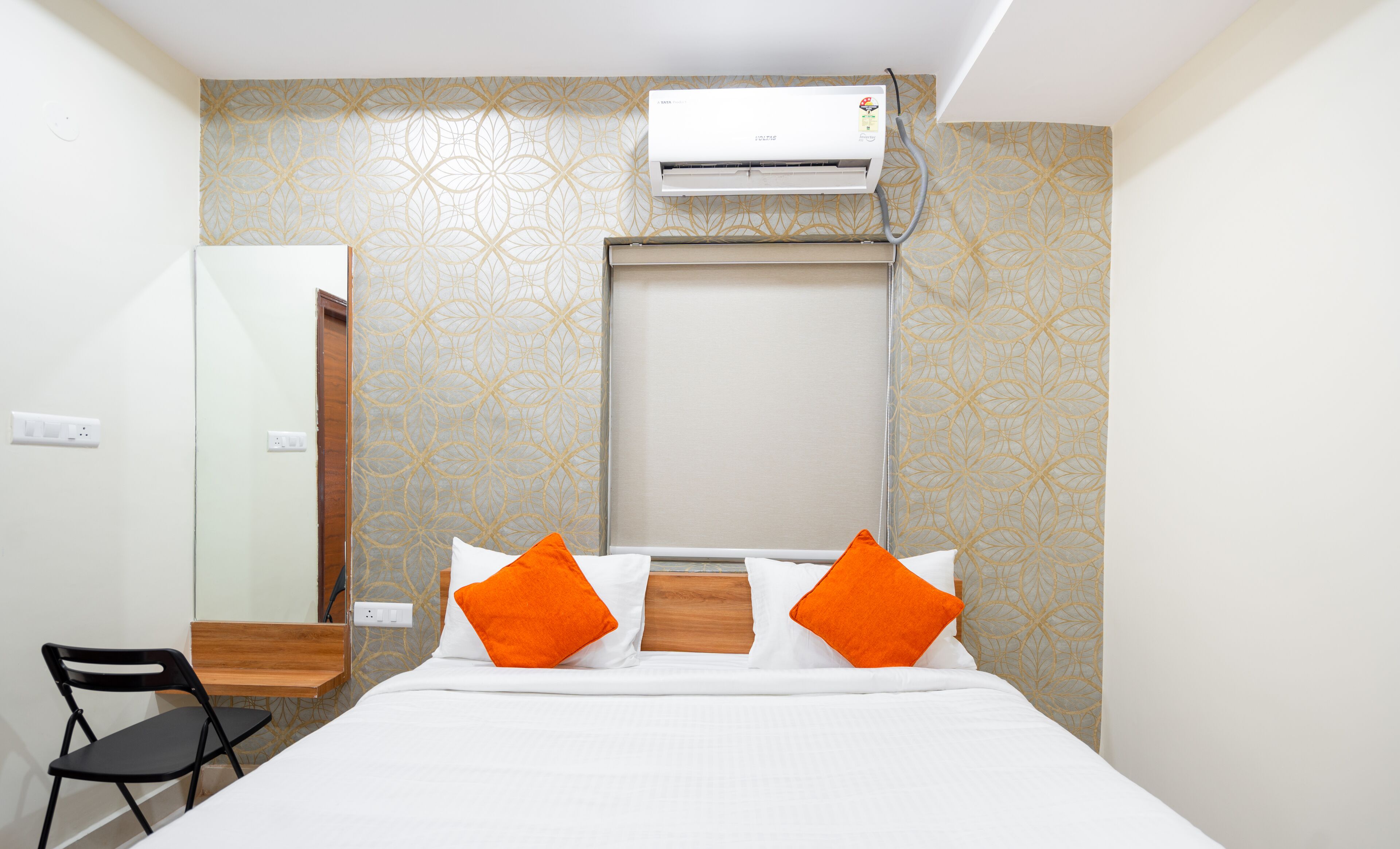 Una camera d'albergo con un letto, un climatizzatore, una scrivania in legno e una sedia.
