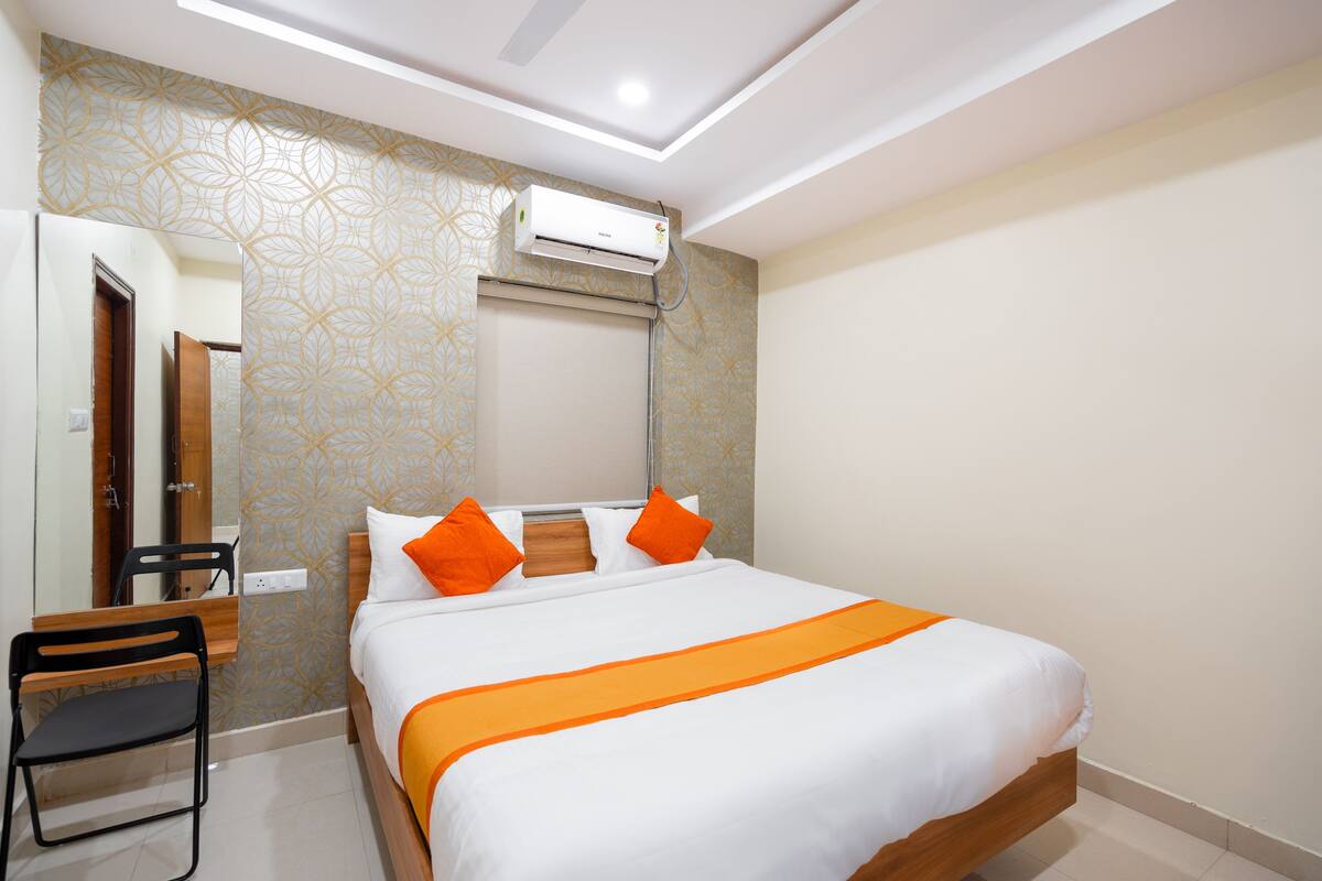 A hotel room with a bed, a desk, a chair, an air conditioning unit, and a mirror.