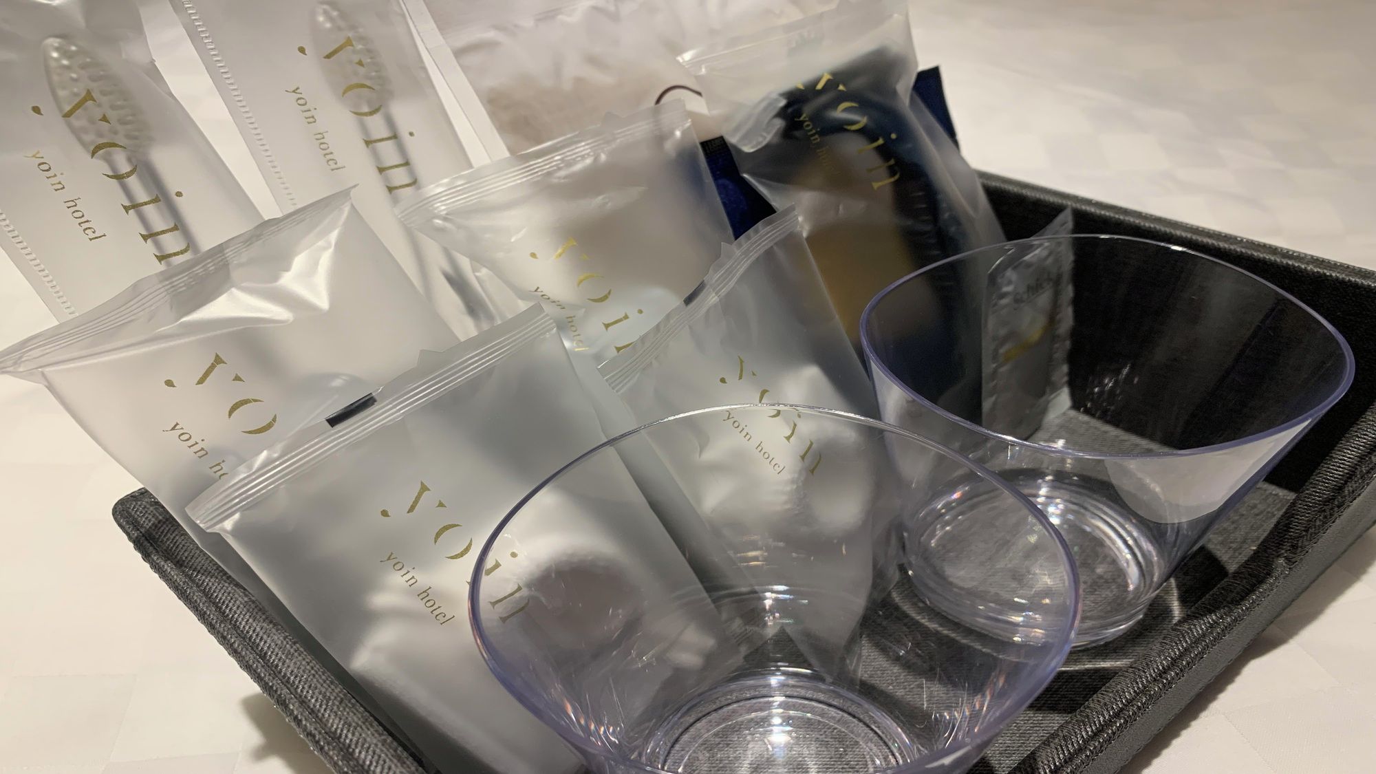 A tray with clear plastic cups and bags with 'yoin hotel' text, suggesting hotel amenities.
