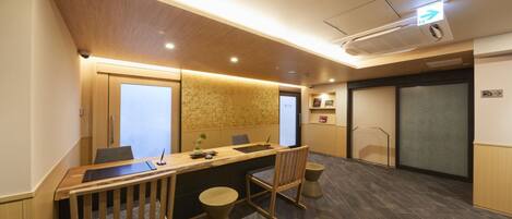 A conference room with a long table, chairs, and a small stool. There are two doors, one with a frosted glass panel and another with a solid panel.