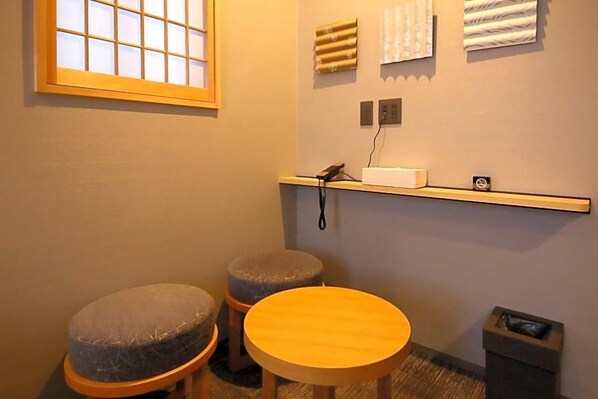 A small bathroom with a window, two stools, a round table, and a shelf with a phone and a trash bin. - Kyoto Gion Hotel (Kyoto)
