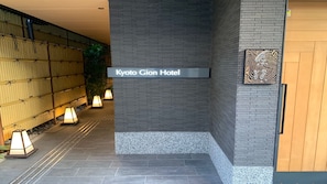 De ingang van Kyoto Gion Hotel, met een bord, een bamboeboog en een decoratieve wand.