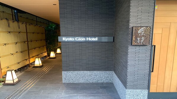 The entrance to Kyoto Gion Hotel with a sign, a bamboo wall, and a patterned wall decoration.