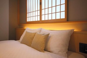 A neatly made bed with white linens and patterned pillows, a wooden headboard, and a window with a grid pattern. - Kyoto Gion Hotel (Kyoto)