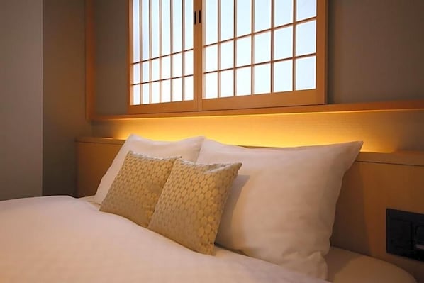Un lit bien fait, avec du linge de lit blanc et des coussins à motifs, une tête de lit en bois et une fenêtre à carreaux.