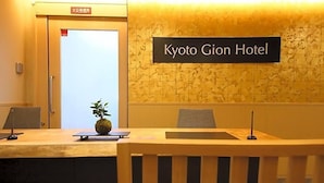 A reception desk at Kyoto Gion Hotel with a sign above it, a potted plant, and a door with an emergency exit sign. - Kyoto Gion Hotel (Kyoto)