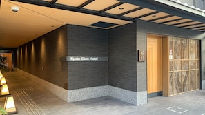 A hotel entrance with a sign reading 'Kyoto Gion Hotel,' a tiled floor, and a door with a patterned glass panel.