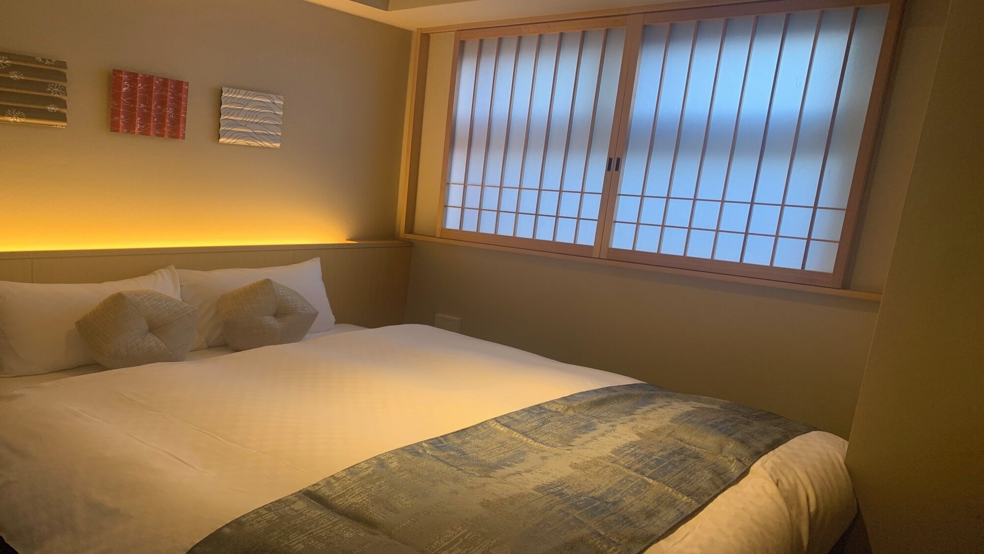 A hotel room with a bed, a window with blinds, and wall art.