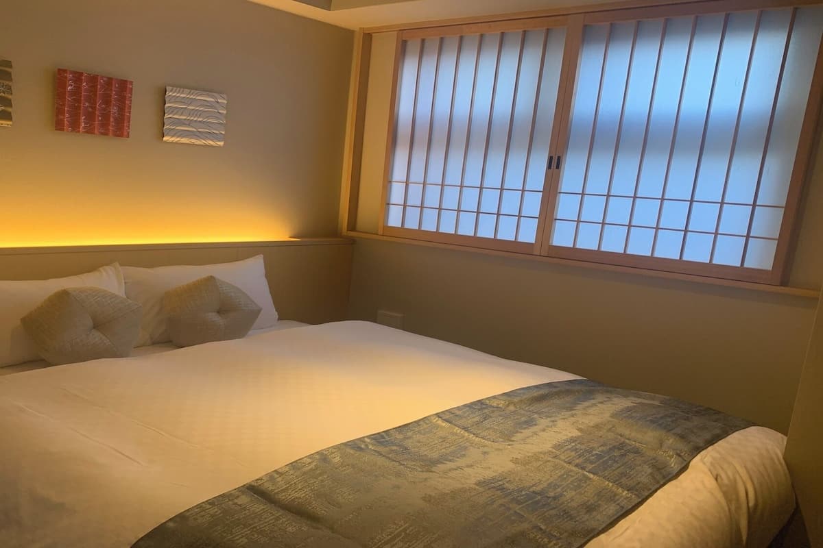 A hotel room with a bed, a window with blinds, and wall art.