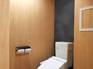 A small, compact bathroom with a toilet, a paper towel dispenser, and a wall-mounted mirror. - Kyoto Gion Hotel (Kyoto)
