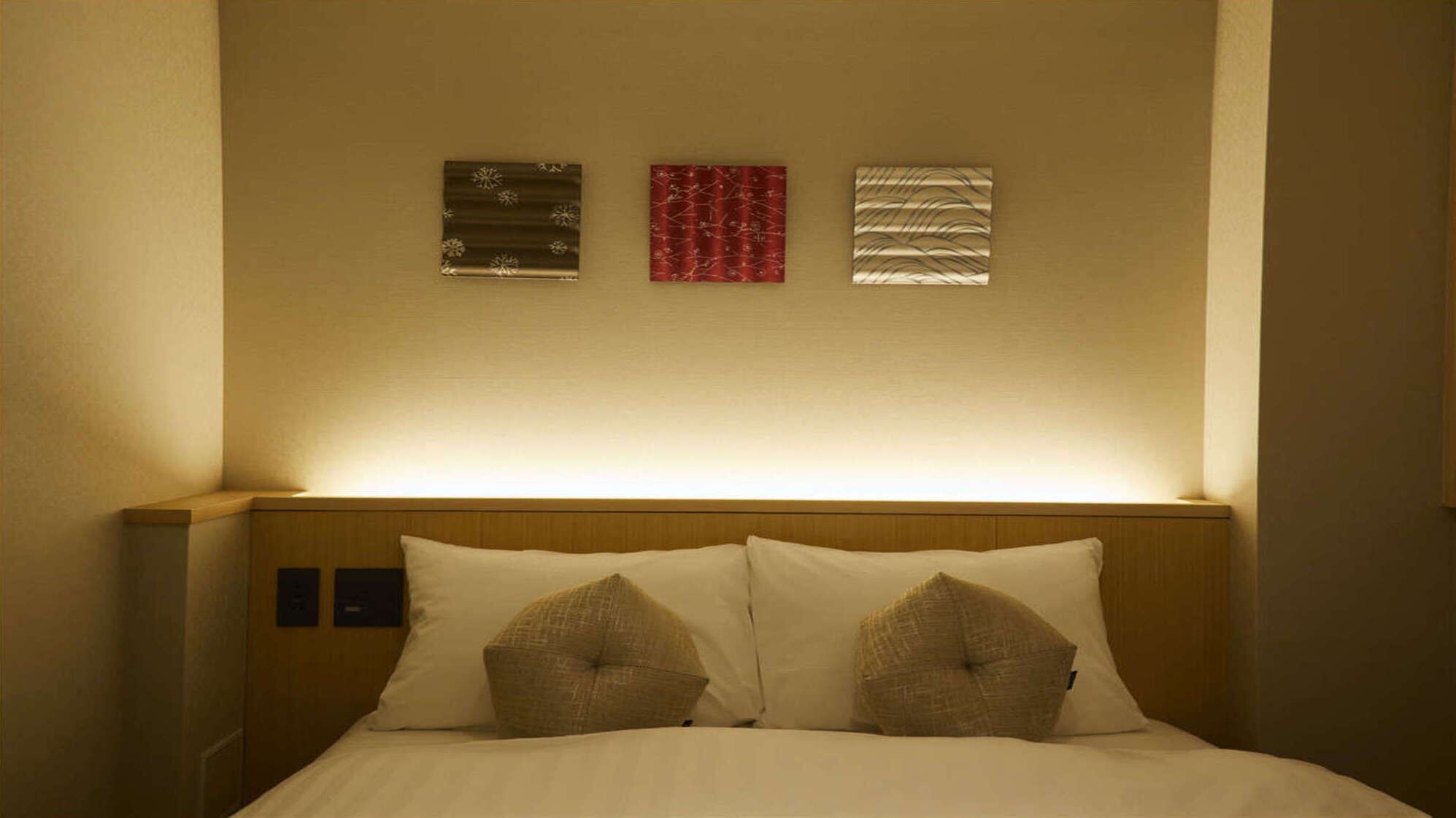Une chambre d’hôtel avec une tête de lit en bois, deux oreillers et trois œuvres d’art accrochées au mur.