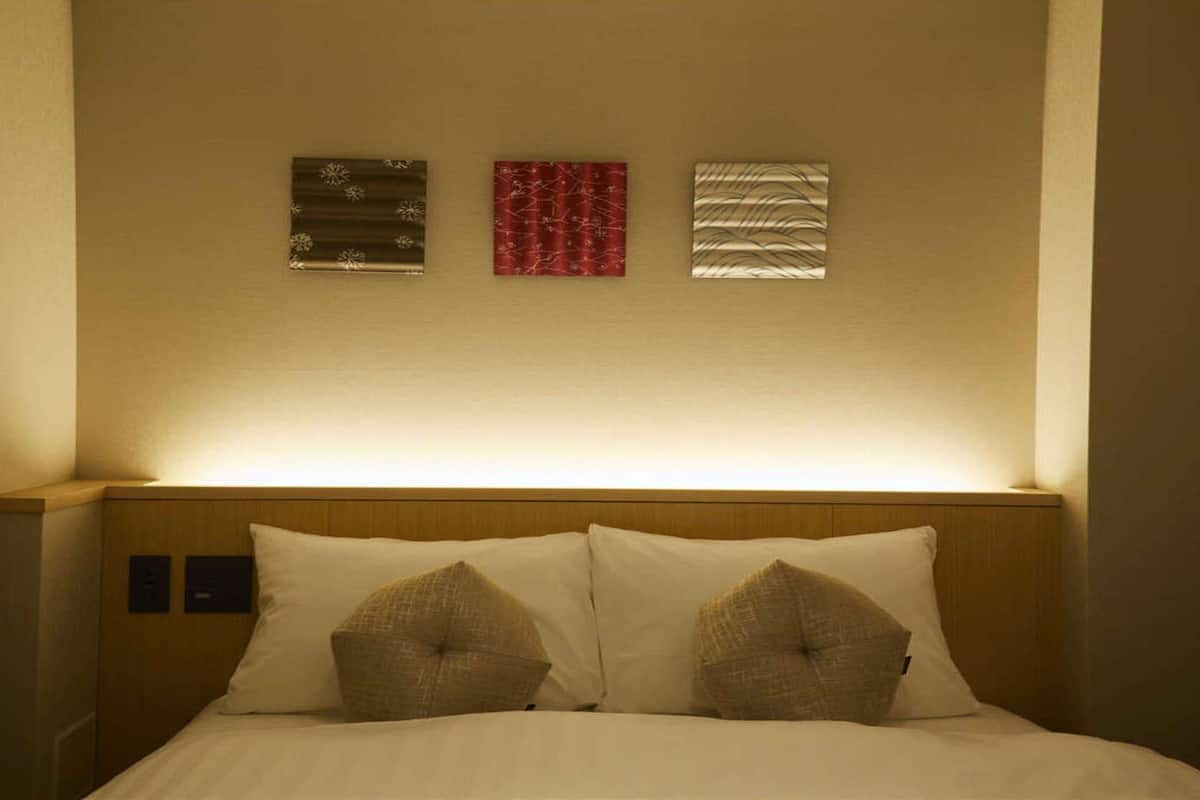 A hotel room with a wooden headboard, two pillows, and three wall-mounted artworks.