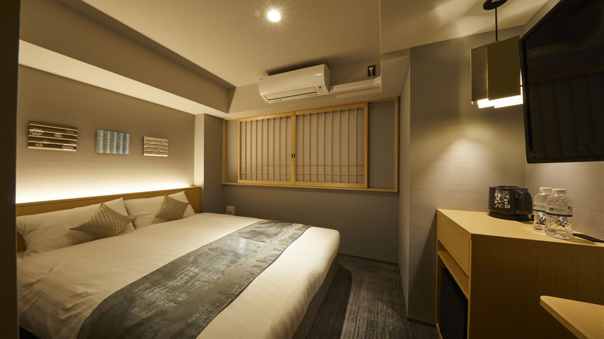 A hotel room with a bed, bedside table, air conditioning unit, and a mirror.