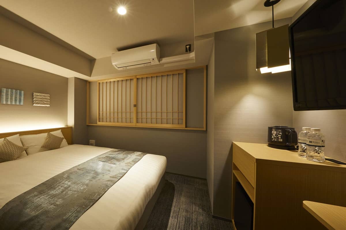 A hotel room with a bed, bedside table, air conditioning unit, and a mirror.