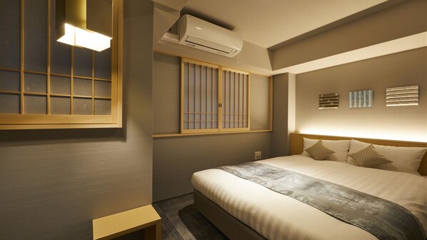 Habitación de hotel con cama, mesita de noche, equipo de aire acondicionado, ventana con persianas y cuadro en la pared.