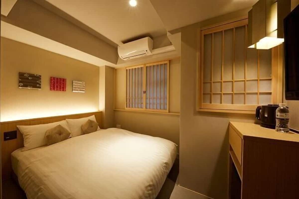A hotel room with a bed, a bedside table, an air conditioning unit, a window with a view, and a wall-mounted air purifier.
