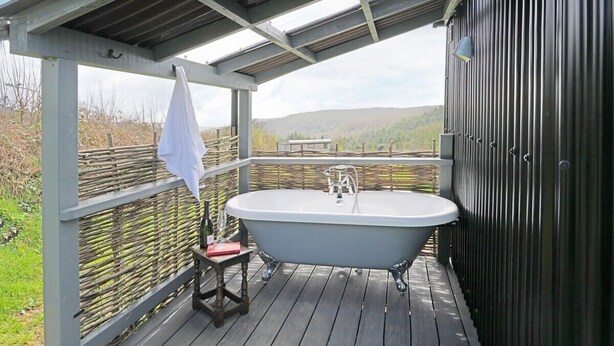 Eine Holzterrasse mit einer freistehenden Badewanne, einem kleinen Tisch und einem Stuhl.