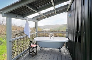 Eine Holzterrasse mit einer freistehenden Badewanne, einem kleinen Tisch und einem Stuhl.
