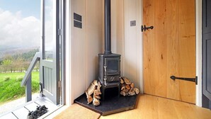 Een houten deur met een zwarte hendel, een kleine zwarte kachel met schoorsteen en een stapel hout.