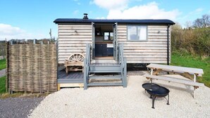 Een klein houten huisje met een veranda, een houten bankje en een barbecue buiten.