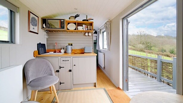 A kitchen with a view of the outdoors, a chair, and a table. - Charming Hut with Outdoor Bath & Decking, Sea Views (Sidmouth)