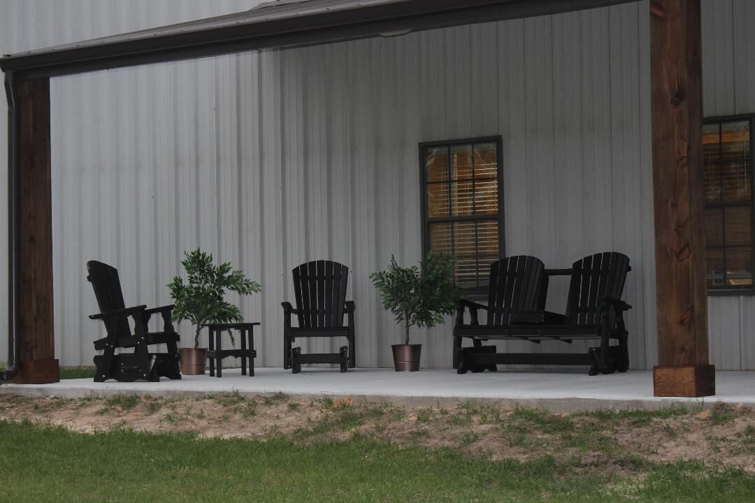 A covered porch with four Adirondack chairs and two potted plants.