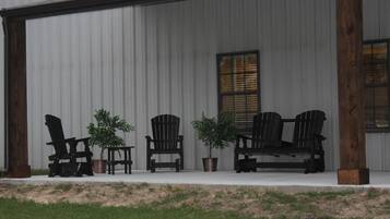 A covered porch with four Adirondack chairs and two potted plants.