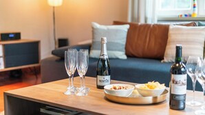 A wooden table with a bottle of RENTUS champagne, three champagne flutes, and bowls of snacks.