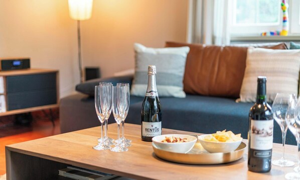A wooden table with a bottle of RENTUS champagne, three champagne flutes, and bowls of snacks.