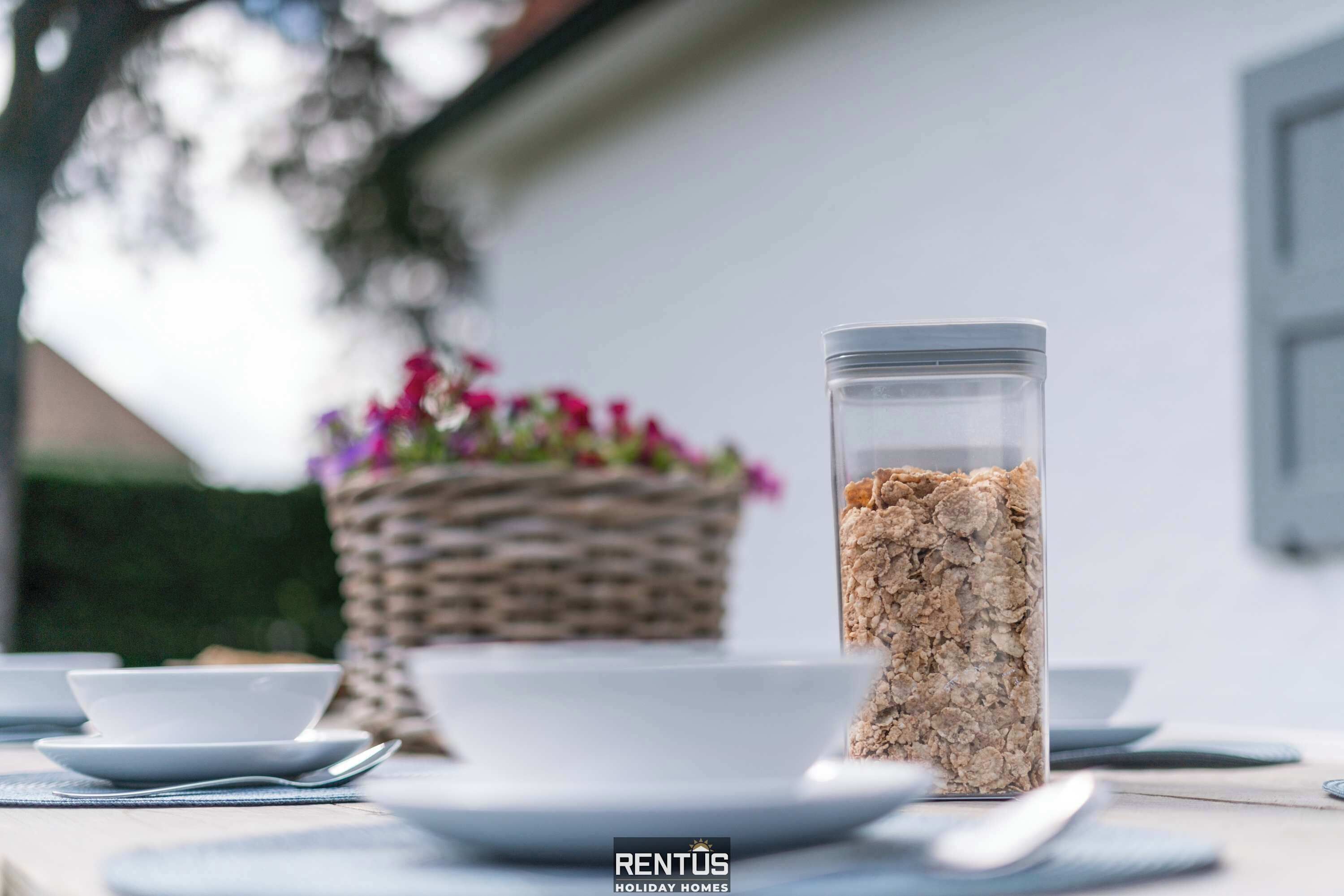 A table with a glass jar of cereal, a bowl, and a spoon.