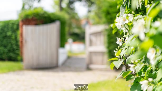 A pathway leading to a gated property with a wooden fence and lush greenery.