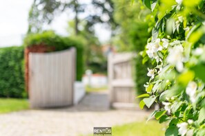 A pathway leading to a gated property with a wooden fence and lush greenery.
