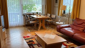 A living room with a sofa, a dining table with chairs, a coffee table, a TV, and a lamp. - Apartment 'Mountain View in Mittenwald' with Balcony, Wi-Fi & Alpine Views (Mittenwald)