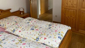 A bedroom with a wooden wardrobe, a bed with floral bedding, and a nightstand with a lamp. - Apartment 'Mountain View in Mittenwald' with Balcony, Wi-Fi & Alpine Views (Mittenwald)
