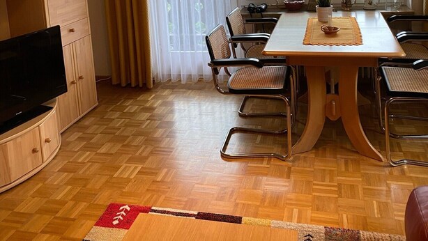A dining area with a table and chairs, a television, and a window with curtains. - Apartment 'Mountain View in Mittenwald' with Balcony, Wi-Fi & Alpine Views (Mittenwald)