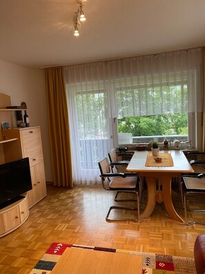 Un comedor con mesa y sillas, un televisor y una ventana con cortinas.