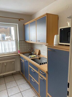Una cocina con armarios azules, microondas, lavamanos y ventana con vistas.