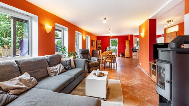 Een moderne woonkamer met een grijze bank, een witte salontafel, en een keuken met een fornuis en kastjes.