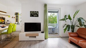 Un salon moderne doté d’un téléviseur à écran plat, d’un canapé, d’un coin repas avec des chaises et d’une grande plante.