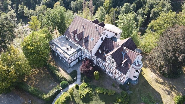 Un grand immeuble à étages, de style architectural traditionnel, entouré d’une forêt dense.