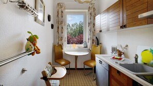 A compact kitchen with a dining table, chairs, a sink, and a window with curtains. - Apartment 'Der Falkenhorst' with Mountain View, Shared Terrace and Wi-Fi (Bad Sachsa)