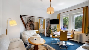 A modern hotel room with a sofa, a round coffee table, a dining table with chairs, a TV, and large windows with curtains. - Apartment 'Der Falkenhorst' with Mountain View, Shared Terrace and Wi-Fi (Bad Sachsa)