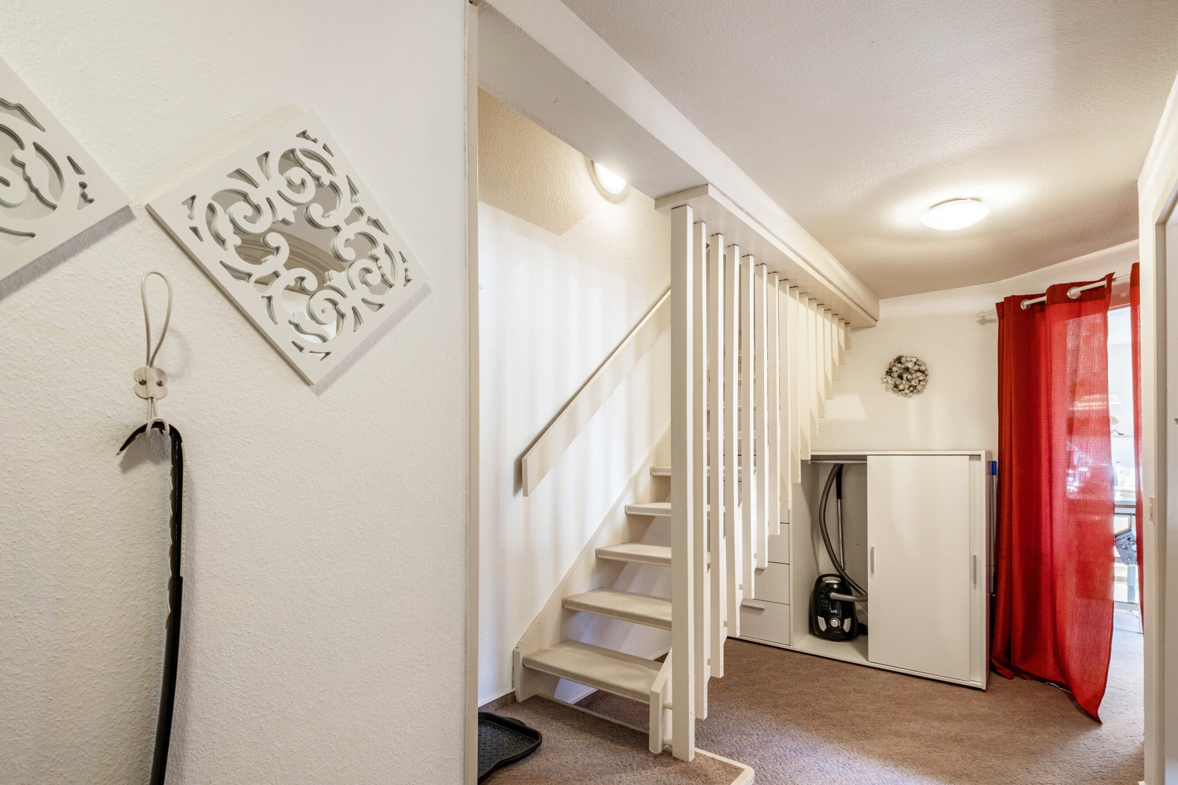 Eine Treppe führt zu einem Raum mit einer weißen Tür, einem roten Vorhang und einem an der Wand befestigten Dekorationsobjekt.