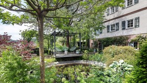 A garden with a pergola, a pond, and a building with multiple windows. - Holiday Home 'Gästehaus Altes Forstamt Sinntal' with Mountain View, Terrace and Wi-Fi (Sinntal)