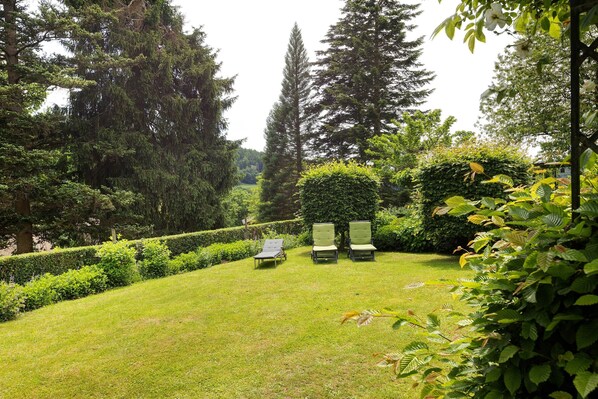 A garden with a lawn, two lounge chairs, and tall trees. - Holiday Home 'Gästehaus Altes Forstamt Sinntal' with Mountain View, Terrace and Wi-Fi (Sinntal)